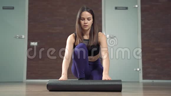 准备瑜伽课的过程年轻快乐的女人在家里或工作室锻炼前滚动垫子视频的预览图