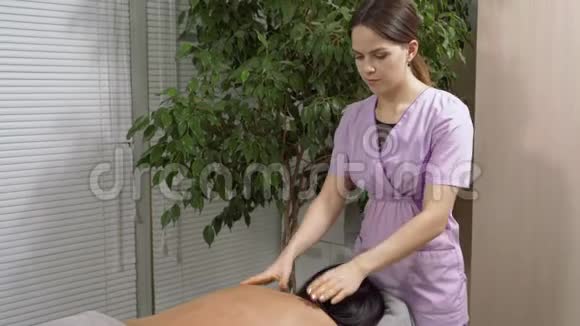 女按摩师在医疗办公室给一个年轻的黑发女人做背部按摩视频的预览图
