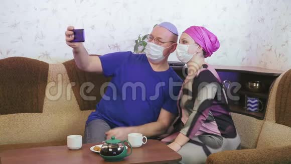 犹太已婚夫妇戴着防护面具在家里沙发上预防冠状病毒视频的预览图