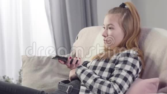 侧视特写的无聊白种人少女坐在沙发和切换频道可爱的少年在看电视视频的预览图