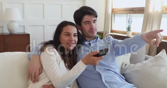 新婚夫妇在沙发上看电视手里拿着遥控器视频的预览图