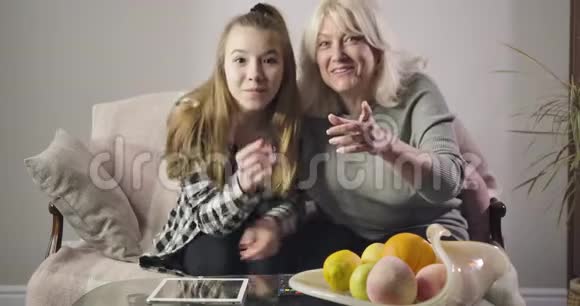 快乐的白人祖母和孙女一起看电视和大笑的肖像积极的家庭开支视频的预览图