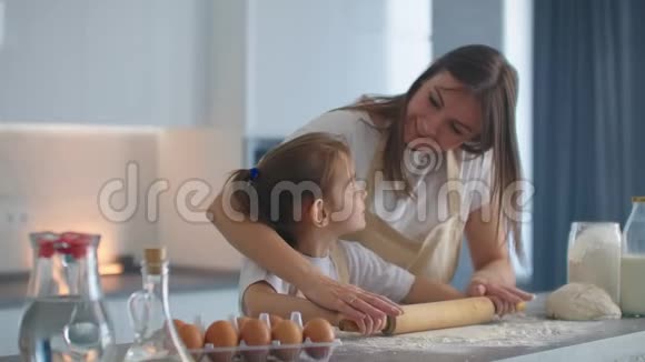 中镜头的母亲和女儿滚动面团在厨房妈妈教女儿做面团女孩学做饭视频的预览图