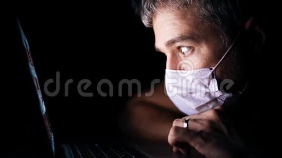 忧心忡忡的男人戴着面罩透过笔记本电脑上的一个新闻网站看最新冠状病毒爆发资讯视频的预览图