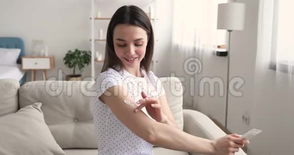 微笑的年轻女子在家的手臂上涂抹保湿乳液视频的预览图