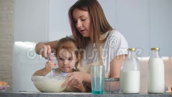 快乐的妈妈和微笑的女儿把面粉和牛奶混合在一起用搅拌器把面团打在碗里视频的预览图
