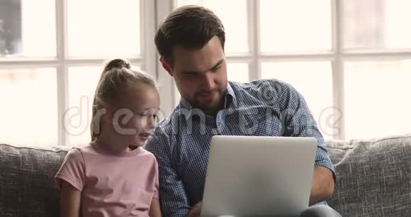 微笑的父亲在笔记本电脑上给小女儿看有趣的视频视频的预览图