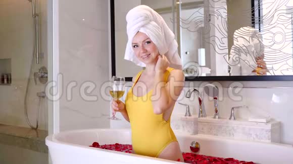 美丽性感的女孩在带红玫瑰花瓣的浴缸里享受着一杯白葡萄酒的乐趣视频的预览图