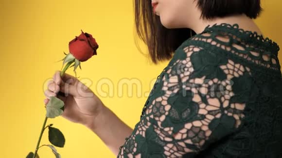 右手拿着红玫瑰的女孩若有所思地嗅着黄色背巾上美丽的花朵2月14日情人节视频的预览图