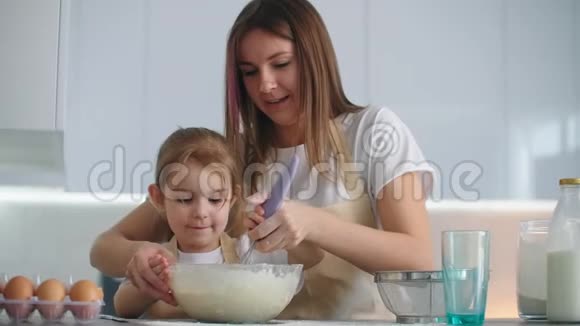 妈妈和女儿站在厨房的围裙里把面团揉在碗里联合休闲家园隔离视频的预览图