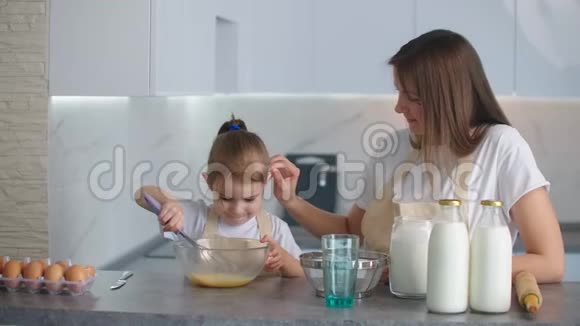 一位母亲看着她的小女儿在厨房里学着穿围裙做饭独立的女儿共享休闲视频的预览图