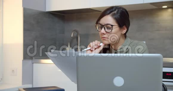 带眼镜的年轻女人在笔记本电脑上工作到很晚在家里准备带文件的报告加班视频的预览图
