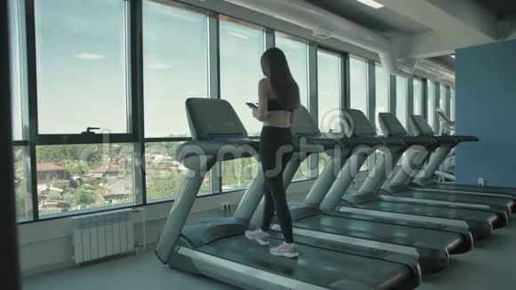 美丽的运动女孩听智能手机音乐应用程序在跑步机上运行视频的预览图