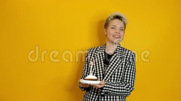 年轻时尚的女士用一块馅饼和蜡烛在黄色背景下庆祝生日视频的预览图