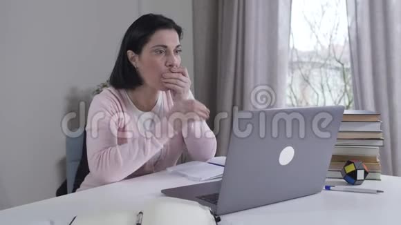 年轻压力大的高加索女人看着笔记本电脑屏幕摇头用手拿着它令人震惊的黑发母亲视频的预览图