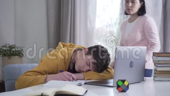 布鲁内特高加索人的母亲来到儿子身边睡在桌子旁叫醒他精疲力竭的十几岁男孩睡着了视频的预览图
