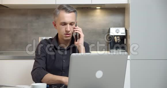 英俊的商人在笔记本电脑上工作在家里的办公室用手机说话自由职业和远程工作理念视频的预览图