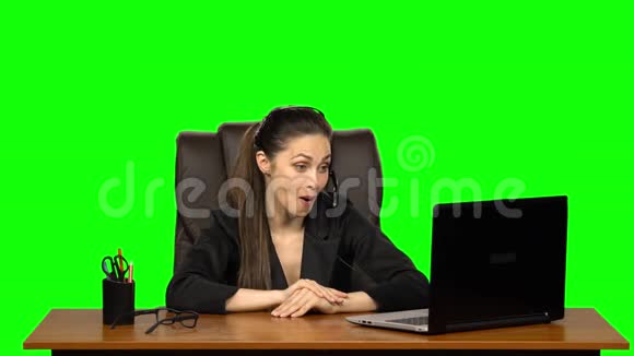 商务女孩戴着耳机用网络摄像头说话带着喜悦的情绪看着笔记本电脑绿色屏幕视频的预览图