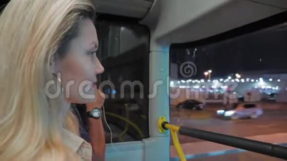 年轻的金发女人乘两层公共汽车穿过夜大都会在道路和棕榈树的背景下视频的预览图