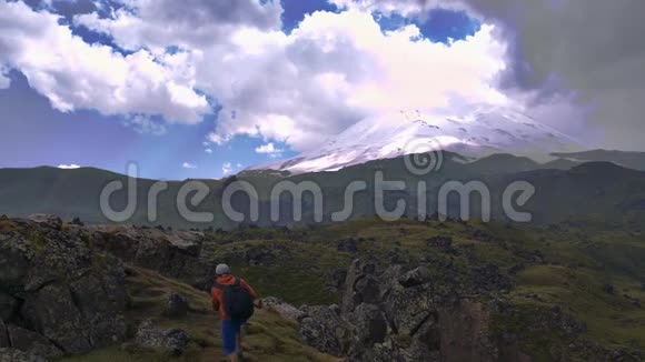 一个带着徒步旅行背包的人在美丽的风景背景上爬上了山那里有高高的悬崖和云彩埃尔布鲁斯视频的预览图