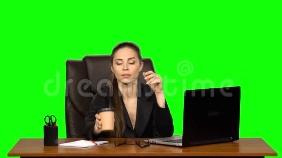 商务女性坐在办公桌前的皮革椅子上喝咖啡绿色屏幕工作室视频的预览图