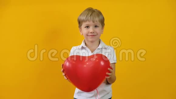 有趣的快乐小男孩蹒跚学步手里拿着红色心形气球在黄色的背景上微笑视频的预览图
