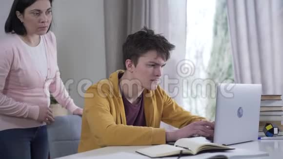 担心的白人妇女偷看笔记本电脑屏幕作为十几岁的男孩使用社交媒体焦急的母亲在跟踪儿子视频的预览图