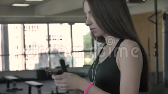 美丽的运动女孩听智能手机音乐应用程序在跑步机上运行视频的预览图