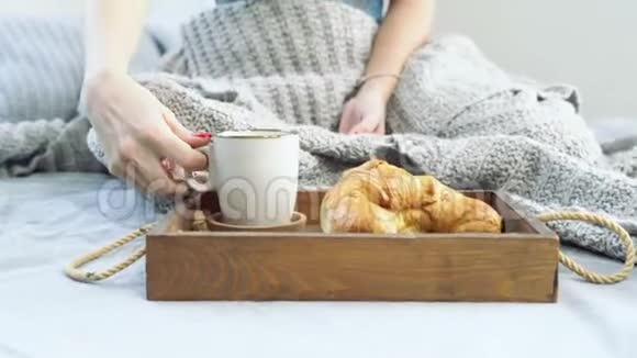 接近一个年轻的女人享受早晨和早餐与羊角面包和咖啡在床上视频的预览图