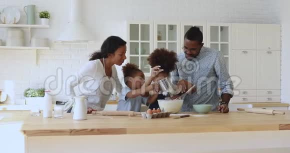 快乐的非洲种族父母看着孩子兄弟姐妹做饭视频的预览图