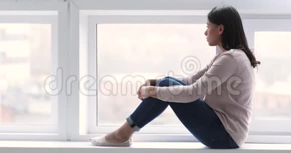 体贴的非裔美国女人坐在窗台上透过窗户看视频的预览图
