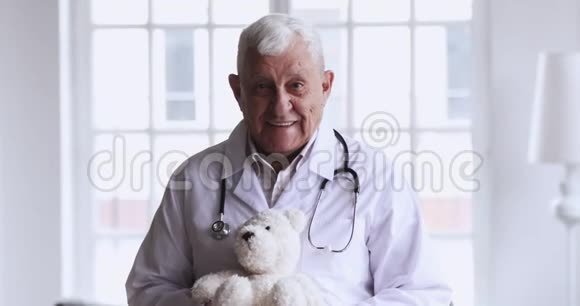 微笑的老男儿科医生抱着泰迪熊看着相机视频的预览图