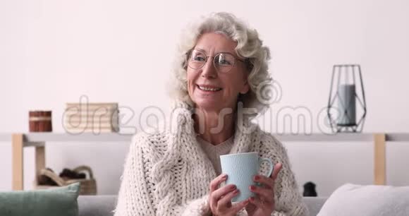 微笑的老妇人看着相机在家喝茶视频的预览图