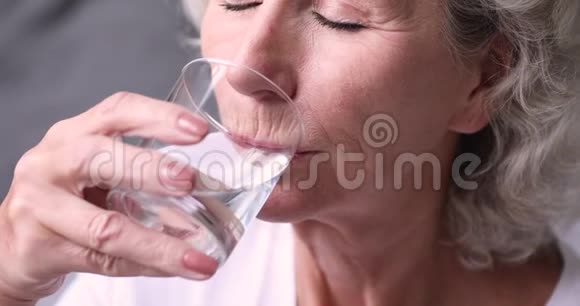 口渴的健康老年妇女拿着玻璃饮用水关门视频的预览图