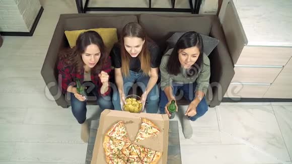 三个年轻的女人喝着啤酒看着电视在她们最喜欢的球队欢呼在家的客厅里为进球而欢呼视频的预览图