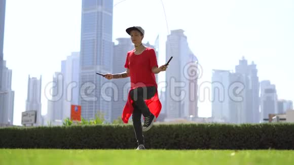 年轻女孩用跳绳在草地上跳跃以迪拜的城市景观为背景视频的预览图