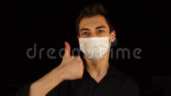 戴医疗面具的年轻人拇指朝上被隔离在黑色上视频的预览图