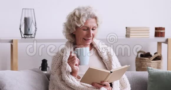 微笑的老妇人看书坐在沙发上喝茶视频的预览图