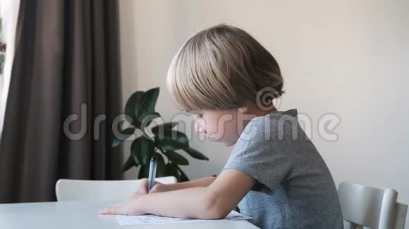 学龄前男孩孩子坐在家里的桌子上画画或做家庭作业视频的预览图