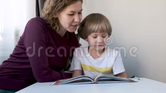 学龄前男孩孩子坐在家里的桌子旁和妈妈一起读书视频的预览图