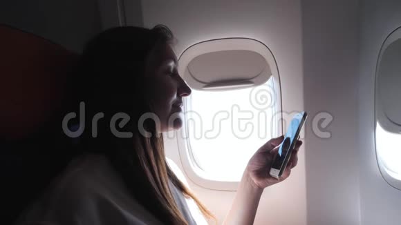 穿着灰色T恤的女士看着手机对着明亮的舷窗视频的预览图
