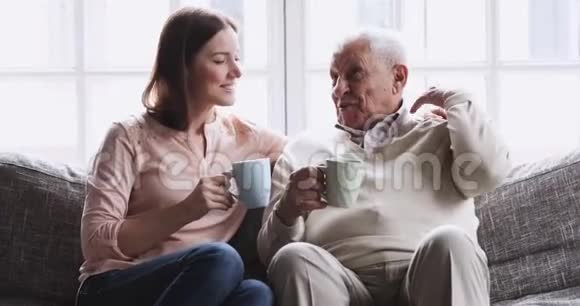 快乐的祖父和孙女在沙发上聊着喝茶视频的预览图