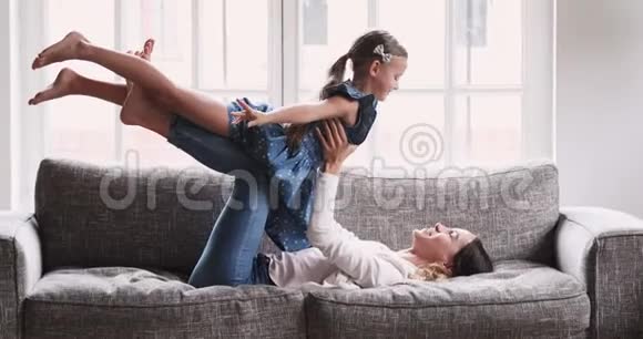 年轻妈妈抱着小女儿在沙发上玩飞机游戏视频的预览图