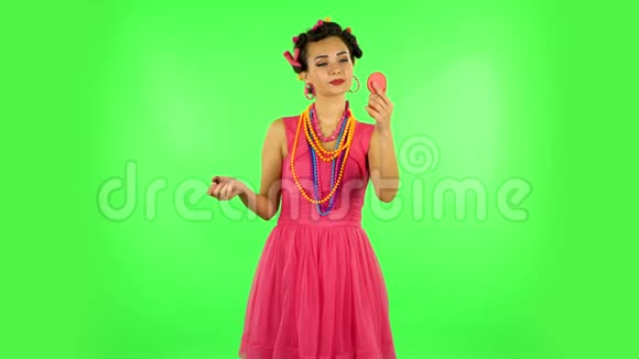 头上戴卷发的女孩穿着一件粉红色的连衣裙她的嘴唇在红色的镜子里绿色屏幕视频的预览图