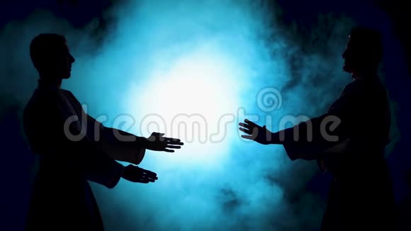 两名练习合气道技术的战士在黑暗的工作室里的主人的轮廓与烟雾和灯光慢动作视频的预览图
