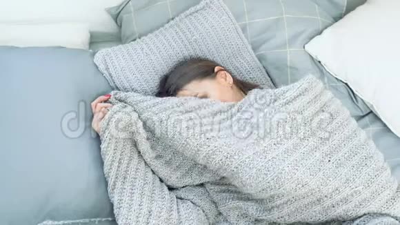 一个年轻漂亮的女人从毯子下偷看在家里的床上享受早晨的肖像视频的预览图