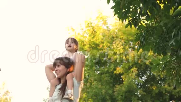 妈妈把她心爱的孩子扛在肩上在公园里妈妈和女儿一起走在树下的肩膀上视频的预览图