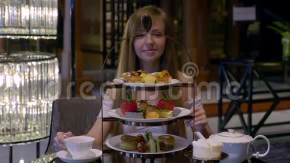有魅力的年轻女孩在餐厅吃盘子里的蛋糕咬肉和喝茶视频的预览图