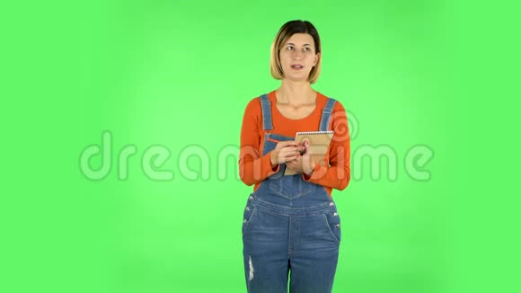 女孩站着思考然后专心地用铅笔在笔记本上写绿色屏幕视频的预览图