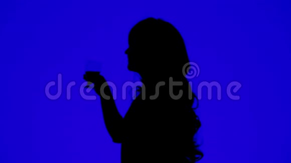 一个卷发女人在蓝色背景下喝着杯子里的酒的剪影视频的预览图